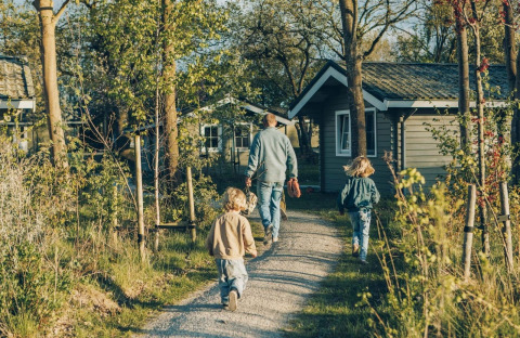 Gezin wandelt op het pad naar het Zweeds Dorp Huis bij Camping De Kleine Wereld, Nederland, tussen natuur.