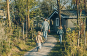 Famiglia che cammina verso la casa svedese al Camping De Kleine Wereld nei Paesi Bassi, circondata dalla natura.