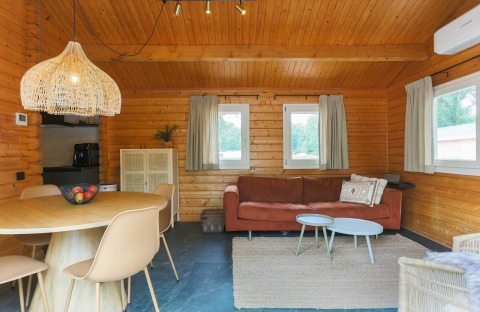 Interno di lodge accogliente con pareti in legno, tavolo rotondo, divano, tappeto e finestre con tende.