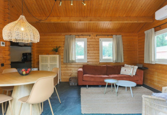 Cozy lodge interior with wood-paneled walls, round dining table, sofa, rug, and three curtained windows.