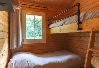 Cozy lodge room with wooden walls, a bunk bed, and a window offering a green view outside in daylight.
