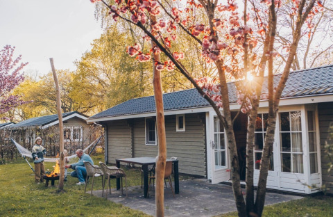 Spring day at Swedish Country Cottage at Camping De Kleine Wereld, Netherlands, with fire pit and flowers.