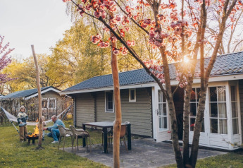 Spring day at Swedish Country Cottage at Camping De Kleine Wereld, Netherlands, with fire pit and flowers.