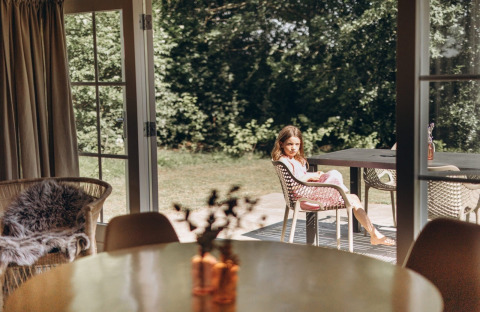 Ragazza seduta fuori a un tavolo presso Swedish Country Cottage a Camping De Kleine Wereld, Paesi Bassi.