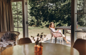 Ragazza seduta fuori a un tavolo presso Swedish Country Cottage a Camping De Kleine Wereld, Paesi Bassi.