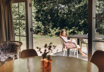 Girl sitting outside at a table at Swedish Country Cottage, Camping De Kleine Wereld, Netherlands.