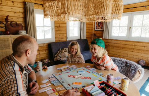 Family playing Monopoly in a Swedish country cottage with sofa bed at Camping De Kleine Wereld, Netherlands.