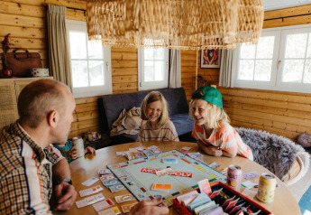 Family playing Monopoly in a Swedish country cottage with sofa bed at Camping De Kleine Wereld, Netherlands.