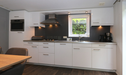 Moderne Küche mit weißen Schränken, Fenster, Geräten und Esstisch in L-Pavilion 6, De Achterhoek, Niederlande.