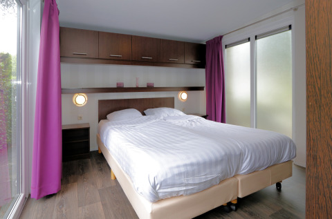 Modernes Schlafzimmer im L-Pavilion 6 in De Achterhoek, Niederlande, mit Doppelbett und lila Vorhängen.