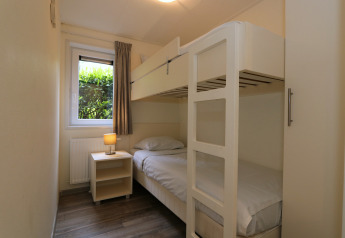 Slaapkamer met stapelbed, nachtkastje en raam met tuinzicht in Pavilion 6 van De Achterhoek, Nederland.