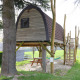 Ein charmantes Baumhaus namens Treelodge, auf Stelzen, mit Treppe und Hängematte darunter im Grünen.
