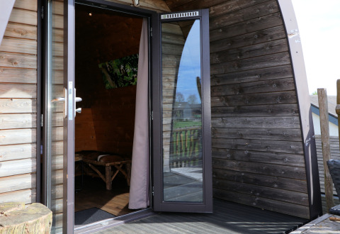 Åben dør til træhytte 'Treelodge' på Gulperberg, Nederlandene, med udsigt til terrassen.