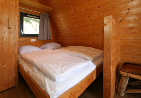 Slaapkamer in de Treelodge boomhut bij Gulperberg, Nederland, met een tweepersoonsbed en houtwanden.