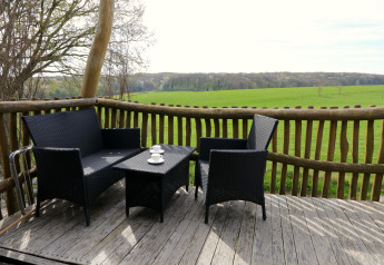 Terrasse avec mobilier de jardin noir et vue sur les champs verts depuis la cabane Treelodge à Gulperberg, Pays-Bas.