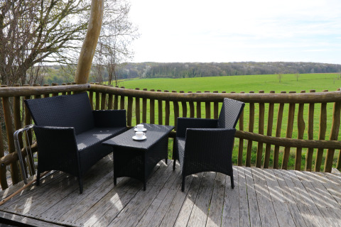 Terras met zwarte tuinmeubelen en uitzicht op groene velden bij Treelodge boomhut in Gulperberg, Nederland.