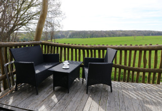 Terrasse med sort havemøbler og udsigt over grønt landskab fra Treelodge treehouse i Gulperberg, Holland.