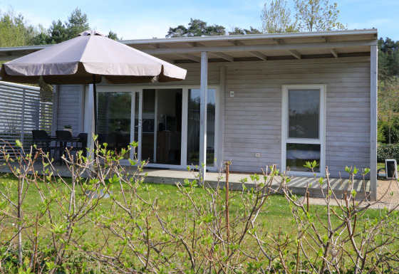 Cosy Unique-lodge met overdekt terras, tuinmeubilair, grote parasol en groene tuin omgeven door natuur.