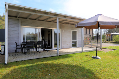 Buitenaanzicht van lodge 'Cosy Unique' in Maasduinen, Nederland, met veranda en parasol.
