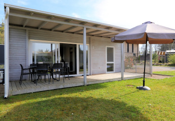 Außenansicht der Lodge 'Cosy Unique' in Maasduinen, Niederlande, mit Terrasse und Sonnenschirm.