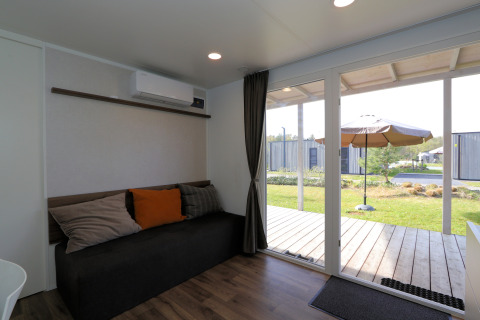 Woonkamer van lodge Cosy Unique in Maasduinen, Nederland, met bank en uitzicht op terras door glazen schuifdeur.