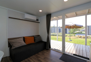 Woonkamer van lodge Cosy Unique in Maasduinen, Nederland, met bank en uitzicht op terras door glazen schuifdeur.