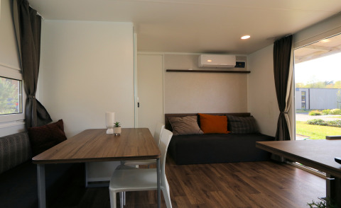 Lichte woonkamer van lodge Cosy Unique in Maasduinen, Nederland, met eettafel, bank en veel ramen.