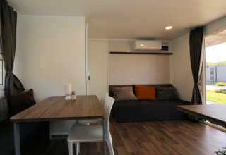 Lichte woonkamer van lodge Cosy Unique in Maasduinen, Nederland, met eettafel, bank en veel ramen.