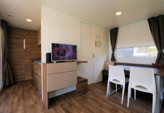 Moderne woonkamer in lodge Cosy Unique in Maasduinen, Nederland, met eettafel, tv en houten vloer.