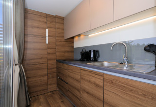 Moderne keuken met houten kasten en grijs aanrecht in lodge «Cosy Unique» in Maasduinen, Nederland.