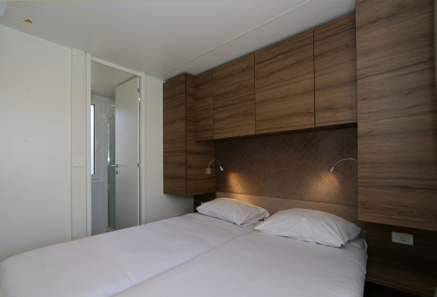 Slaapkamer in Cosy Unique-lodge bij Maasduinen, Nederland, met twee bedden en houten kastjes.