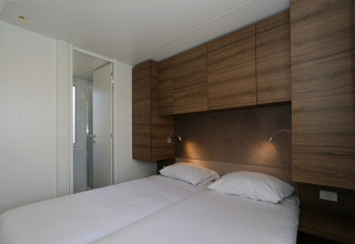 Slaapkamer in Cosy Unique-lodge bij Maasduinen, Nederland, met twee bedden en houten kastjes.