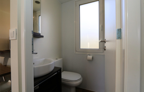 Modern badkamer in lodge 'Cosy Unique' te Maasduinen, Nederland, met wasbak, toilet en raam.