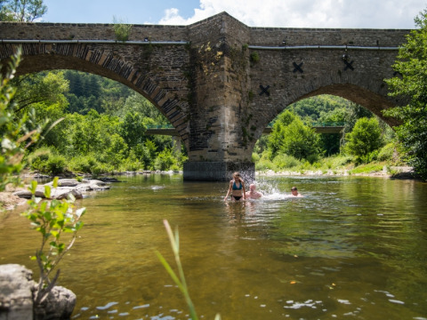 Mensen zwemmen in de rivier onder een stenen brug bij Flower Camping Le Pont du Tarn, Occitanie, Frankrijk.