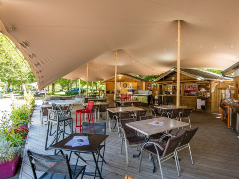 Outdoor seating area with tables and chairs covered by a tent at Flower Camping Le Pont du Tarn, France.