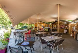 Outdoor seating area with tables and chairs covered by a tent at Flower Camping Le Pont du Tarn, France.