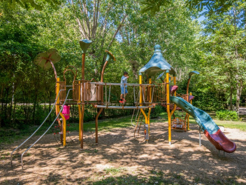 Spielplatz mit Rutsche und Klettergerüst im Grünen auf Flower Camping Le Pont du Tarn in Okzitanien, Frankreich.