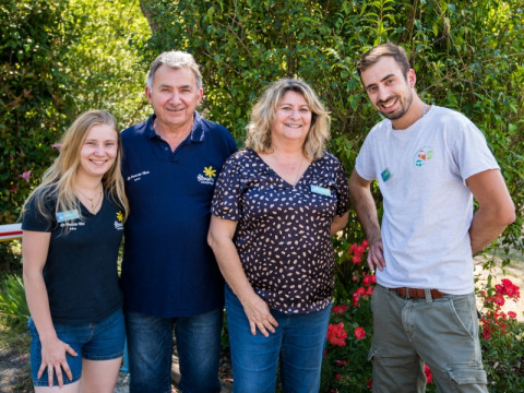 Vier lächelnde Personen stehen vor grünen Büschen im Flower Camping Le Pont du Tarn, Occitanie, Frankreich.