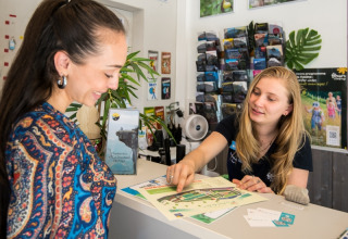 Receptionist assists guest with a map at Flower Camping Le Pont du Tarn holiday park in Occitanie, France.