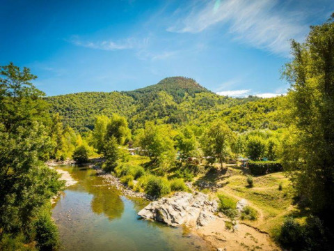 Scenic view of Flower Camping Le Pont du Tarn in Occitanie, France, showing a river, trees, and forested hills.