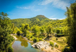 Scenic view of Flower Camping Le Pont du Tarn in Occitanie, France, showing a river, trees, and forested hills.
