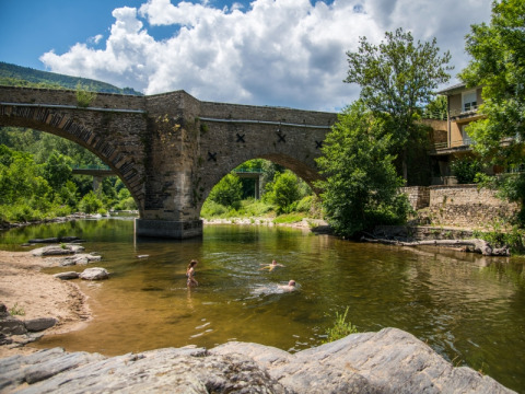 Stone bridge over a river with people swimming at Flower Camping Le Pont du Tarn in Occitanie, France.