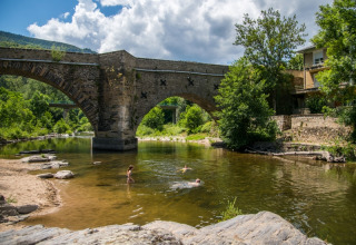Stenen brug over een rivier met zwemmers bij Flower Camping Le Pont du Tarn in Occitanië, Frankrijk.