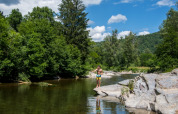 Man op rotsen aan een rivier tussen bomen op Flower Camping Le Pont du Tarn in Occitanië, Frankrijk.