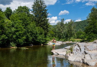 Man op rotsen aan een rivier tussen bomen op Flower Camping Le Pont du Tarn in Occitanië, Frankrijk.