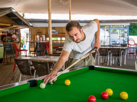 Mand spiller pool ved et bord i et udendørs område på Flower Camping Le Pont du Tarn i Occitanie, Frankrig.