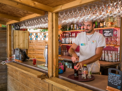 Een barman serveert drankjes aan de houten bar op Flower Camping Le Pont du Tarn in Occitanië, Frankrijk.