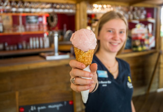 A smiling staff member at Flower Camping Le Pont du Tarn, Occitanie, France, offering an ice cream cone.