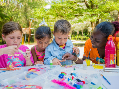 Kinderen gezellig knutselen met een begeleider in de buitenlucht bij Flower Camping Le Pont du Tarn, Occitanië, Frankrijk.