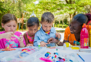 Children and an adult enjoying arts and crafts outdoors at Flower Camping Le Pont du Tarn in Occitanie, France.